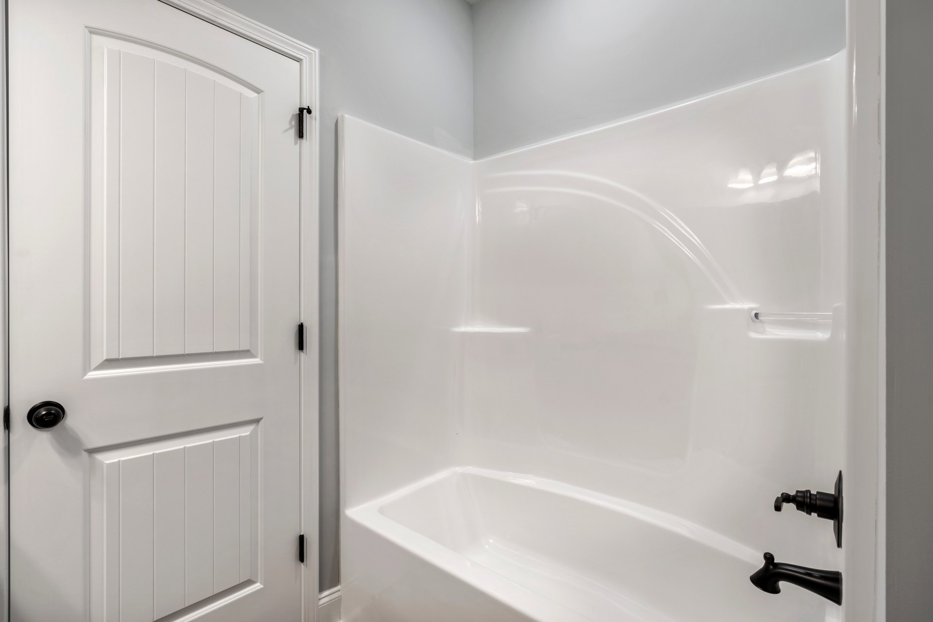 Freestanding white bathtub with matte black faucet beside white cabinet and door with black hardware in a modern bathroom