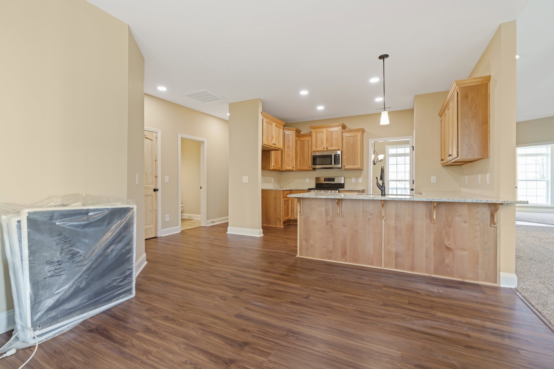 Open kitchen and dining area with wood flooring, white cabinetry, open microwave, black-handled white door, and wooden cabinet close-up; plastic bag with white board visible on