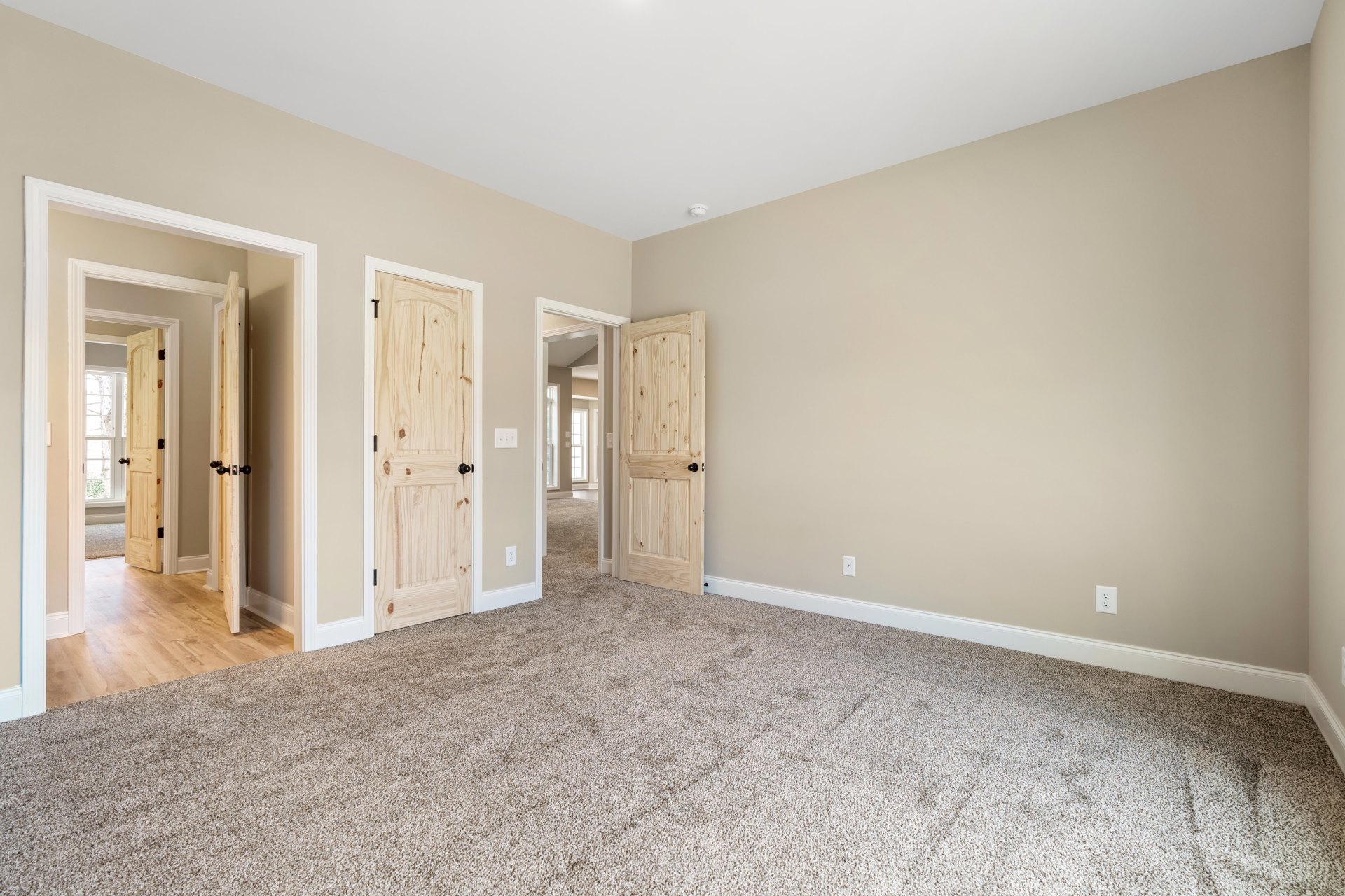 Beige walls with white trim, carpeted floor, open wooden door, and simple interior finishes