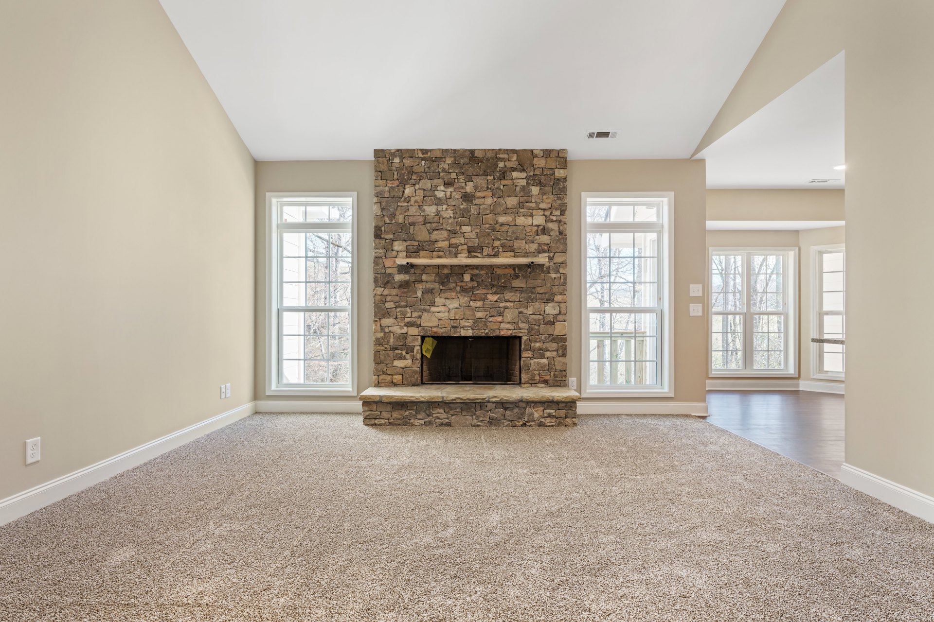 Stone fireplace with black mesh door, built-in wall shelf, tile flooring, multiple windows offering tree views, white plaster walls, crown molding.