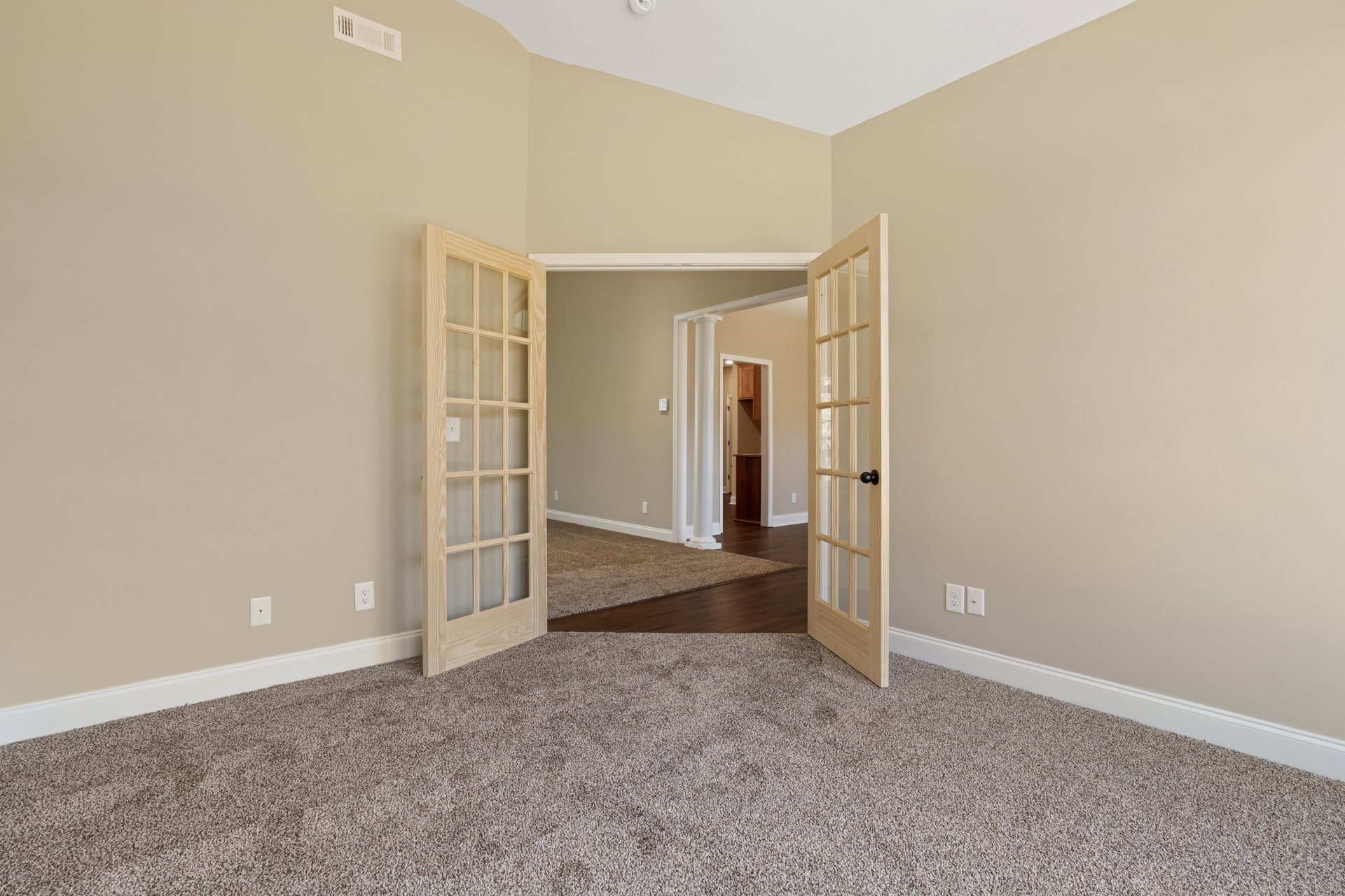 Open white door with glass panes leading from carpeted room to kitchen with stone countertop, white wall vent, and laminate flooring