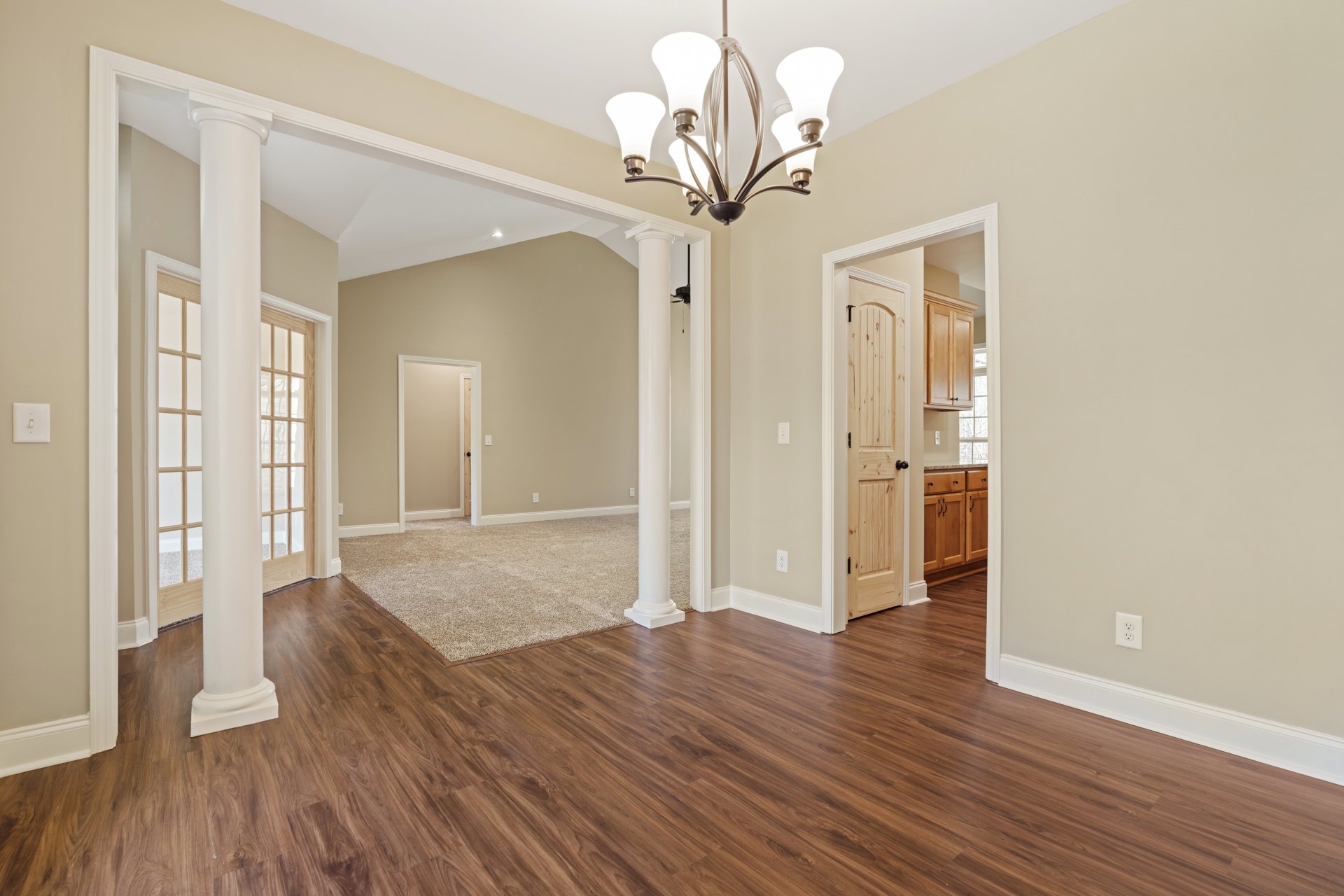Wood floor room with five-light chandelier, white column, white door with black handle, light switch on wall, carpeted area visible