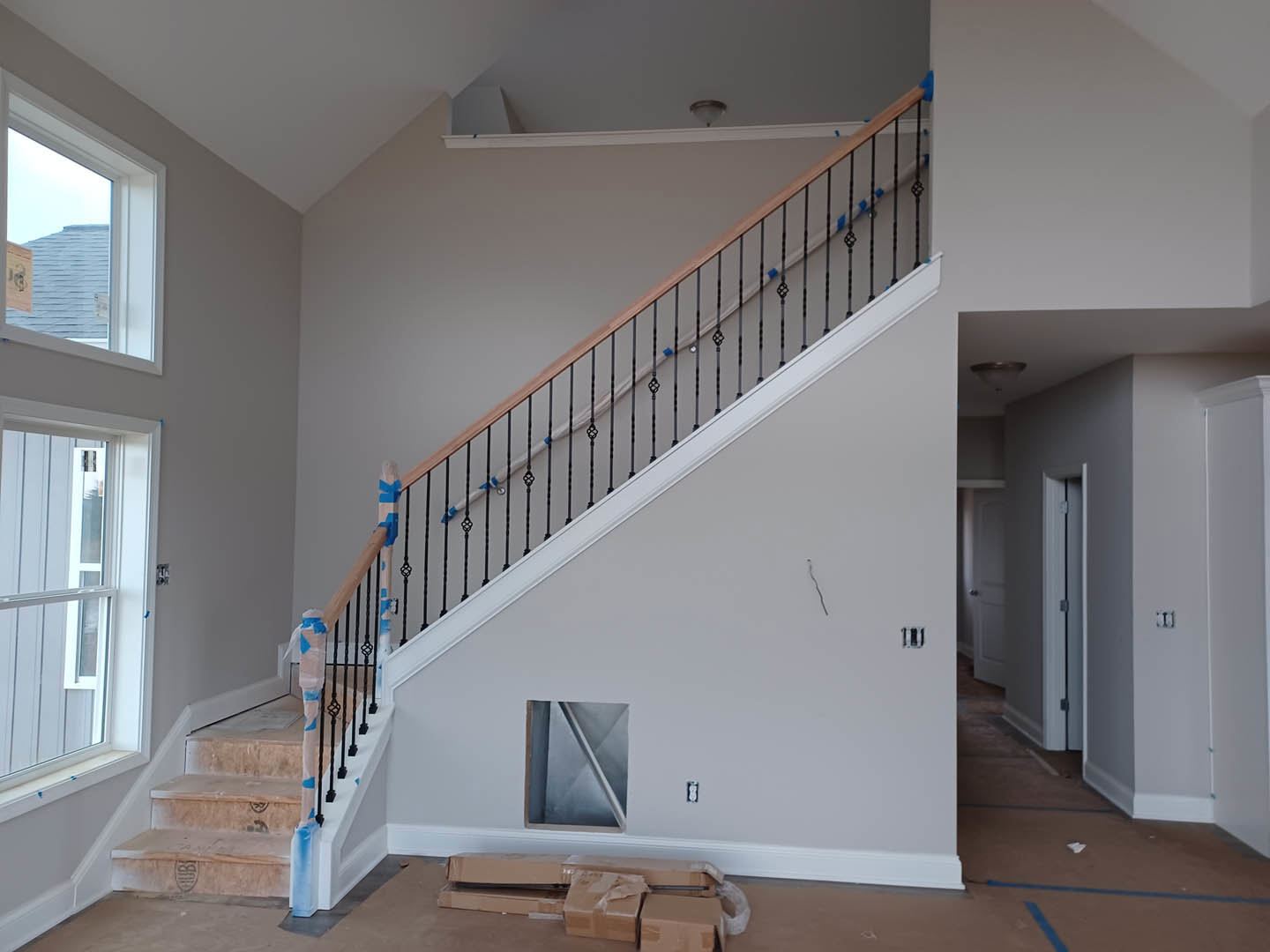 Modern staircase with metal railings, plaster walls, large window, and light wood flooring in a residential interior