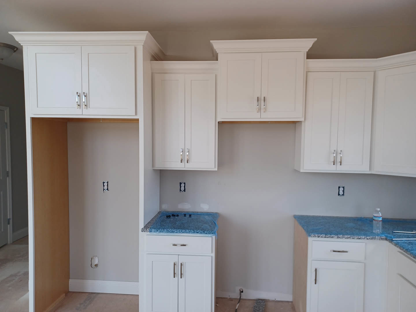 Kitchen with blue countertops, white cabinets with silver handles, white closet doors, stainless steel sink, and a cabinet partially wrapped in plastic.