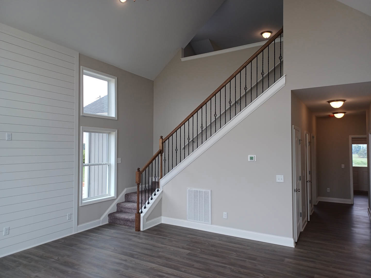 Wood staircase with black metal railing, white walls featuring horizontal paneling, large window with white frame, modern ceiling light fixture, hardwood flooring