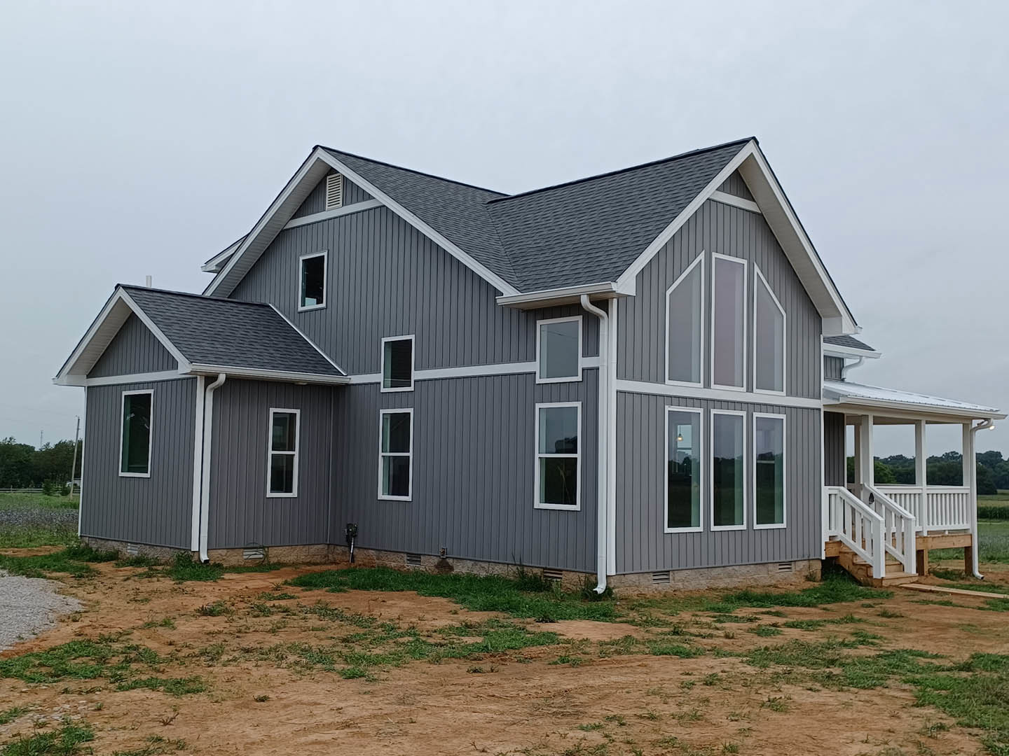 Modern house with light siding, multiple windows, and a large dirt yard bordered by patches of grass
