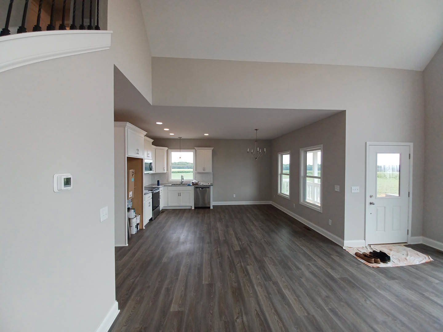 Open living area with light wood flooring, white walls, and a staircase featuring wood treads and white risers; white door with glass window, stainless steel dishwasher, and shoes