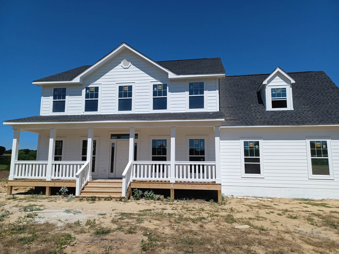 White siding house with covered porch, blue-framed windows, and dirt yard in foreground