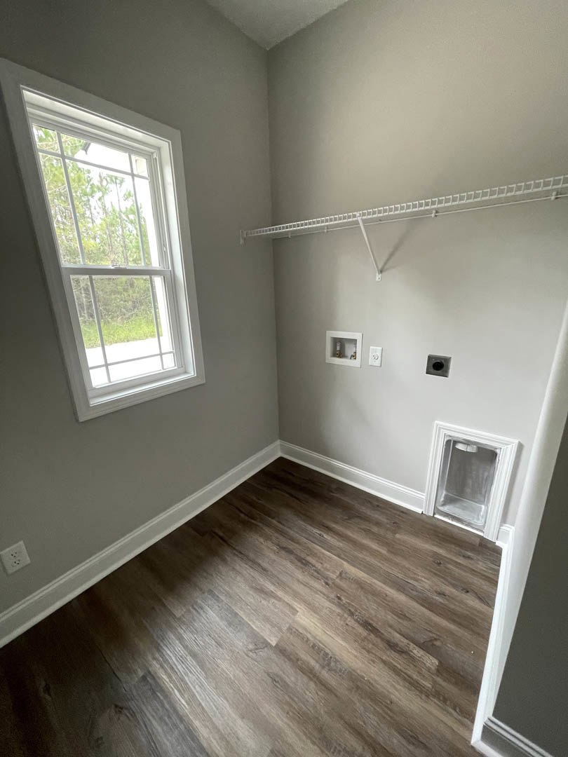 Room with wide plank wood flooring, large window overlooking trees, white ceiling rack, recessed lighting, and smooth plaster walls