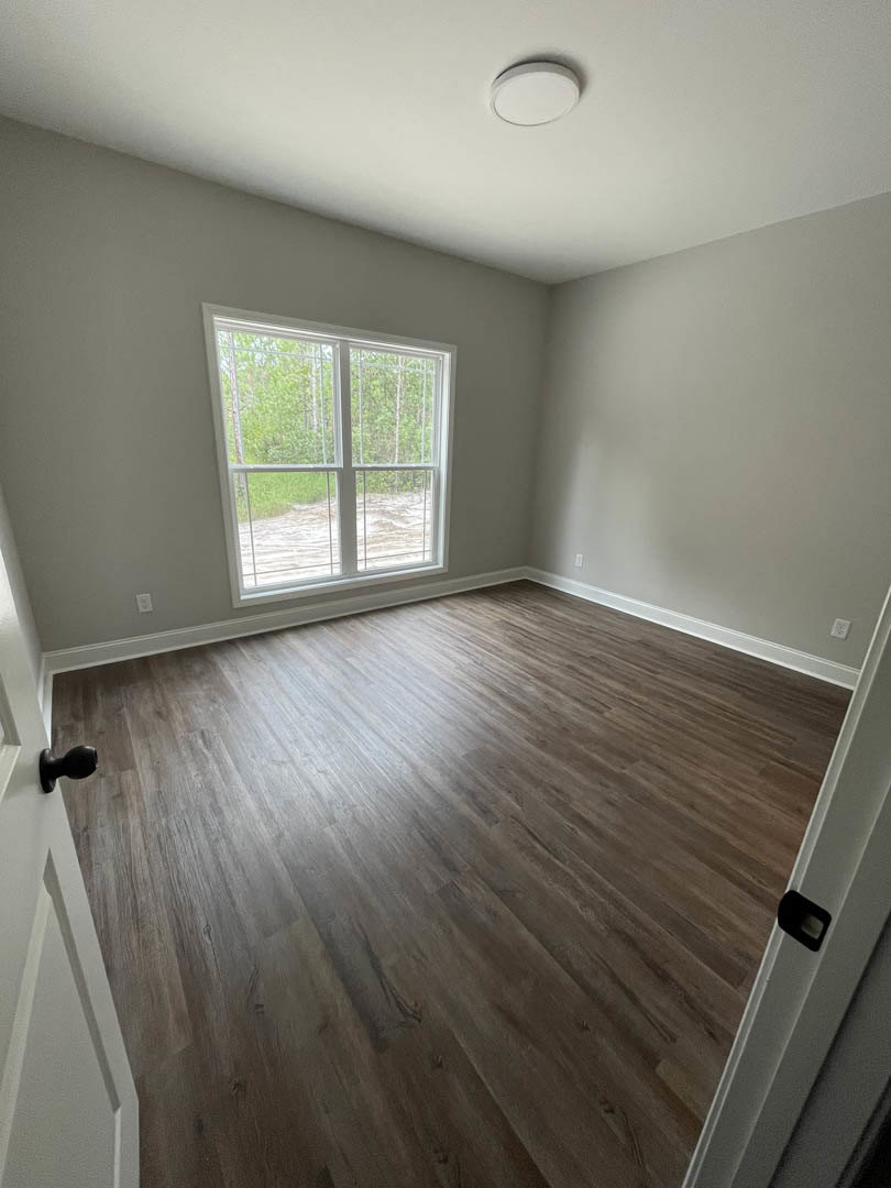 Room with hardwood flooring, plaster walls, large window overlooking trees, and a close-up of a black door handle on a white door