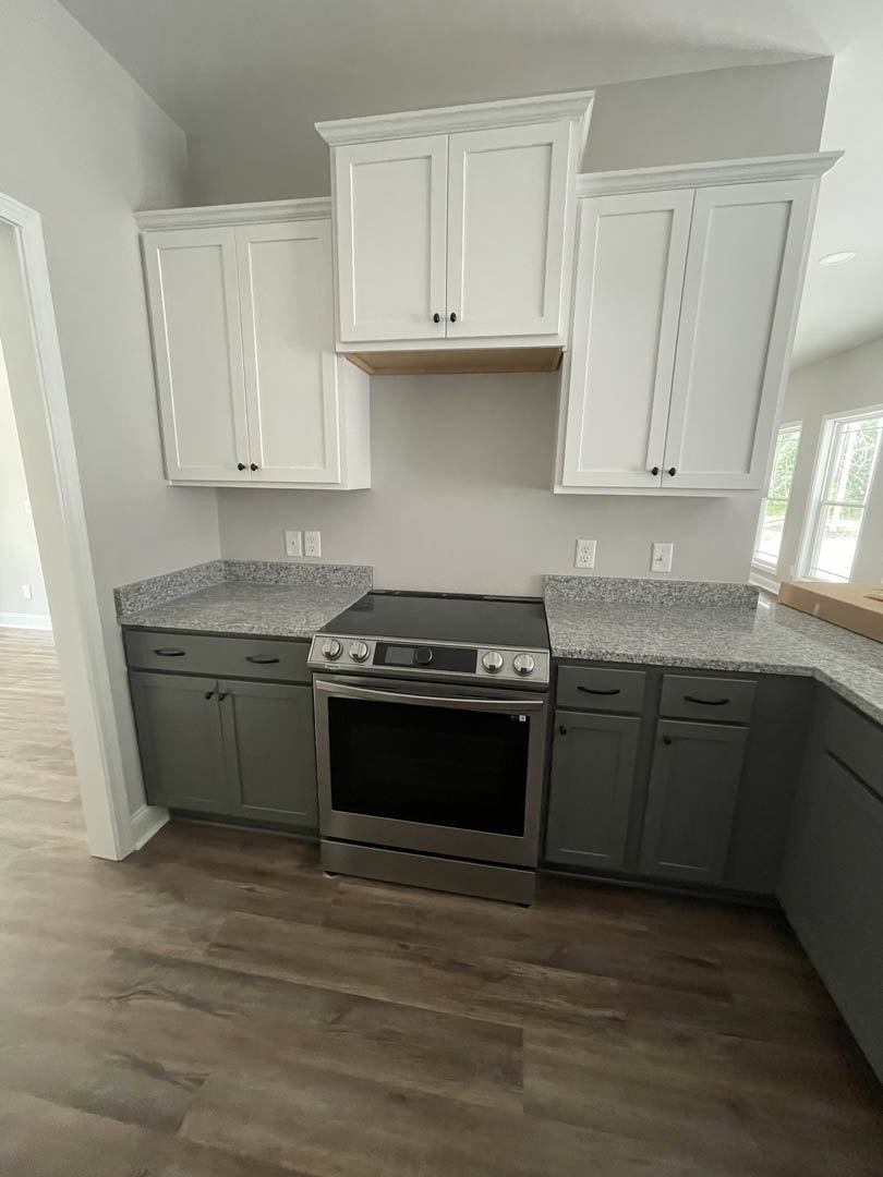 White kitchen with shaker cabinets, grey quartz countertops, stainless steel stove, and light wood flooring