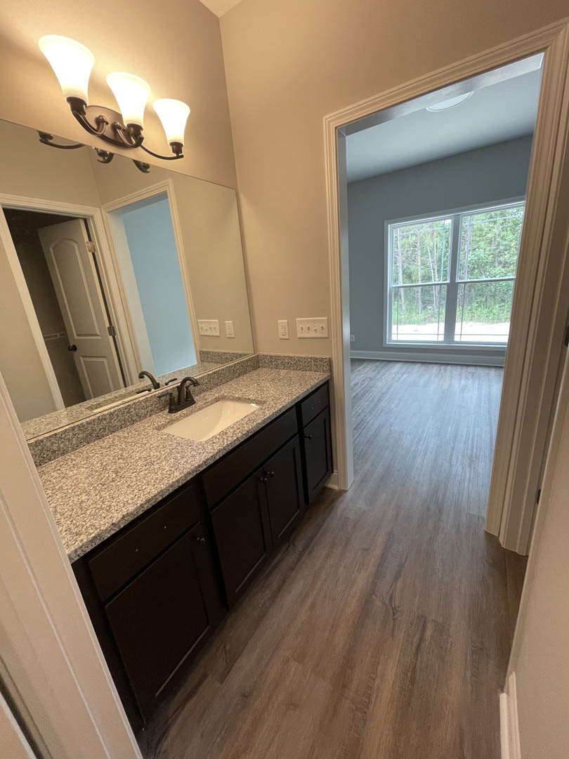 Marble countertop with white sink and black faucet, wood flooring, blue walls with white trim, three-light fixture, window overlooking trees