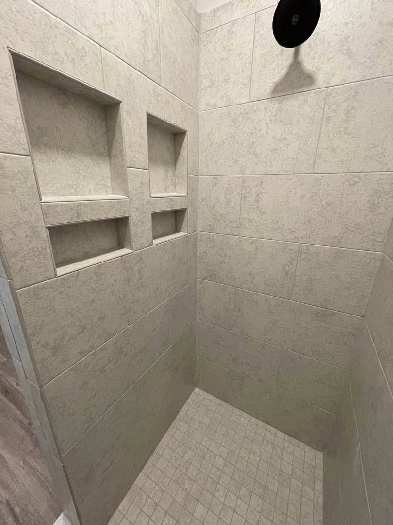 Marble-tiled shower with built-in shelves, chrome shower head, and white wall in modern bathroom.