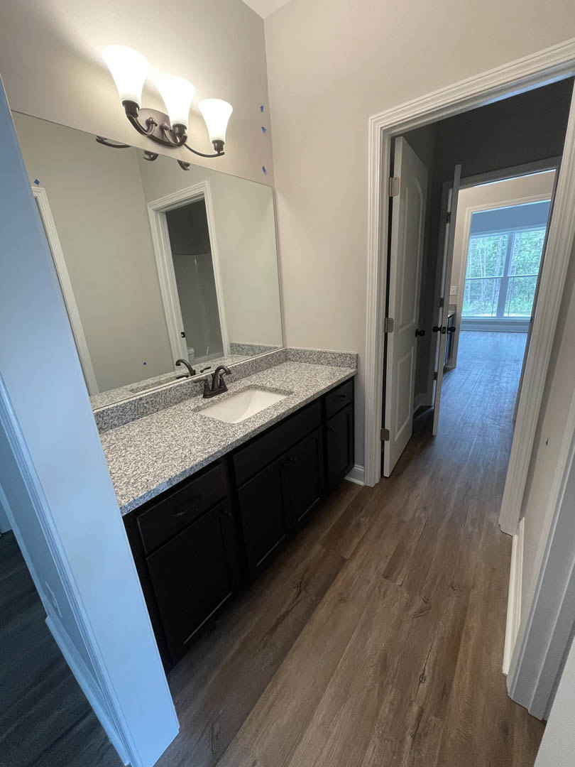 Bathroom featuring marble countertop, white sink with black faucet, wood flooring, close-up of modern light fixture, white-framed door, window overlooking trees, open door leading
