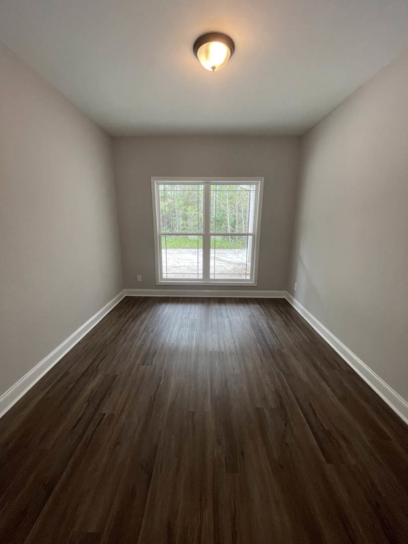 Sunlit room featuring a large window overlooking trees, hardwood flooring, white plaster walls, and a modern ceiling light fixture