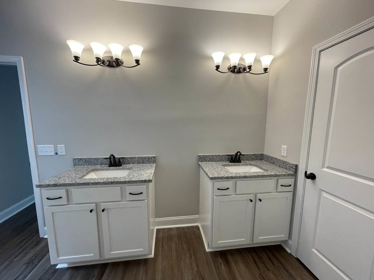 Bathroom with double sinks, black faucets on marble countertops, white cabinetry, three-light fixture above mirrors, and a white door.
