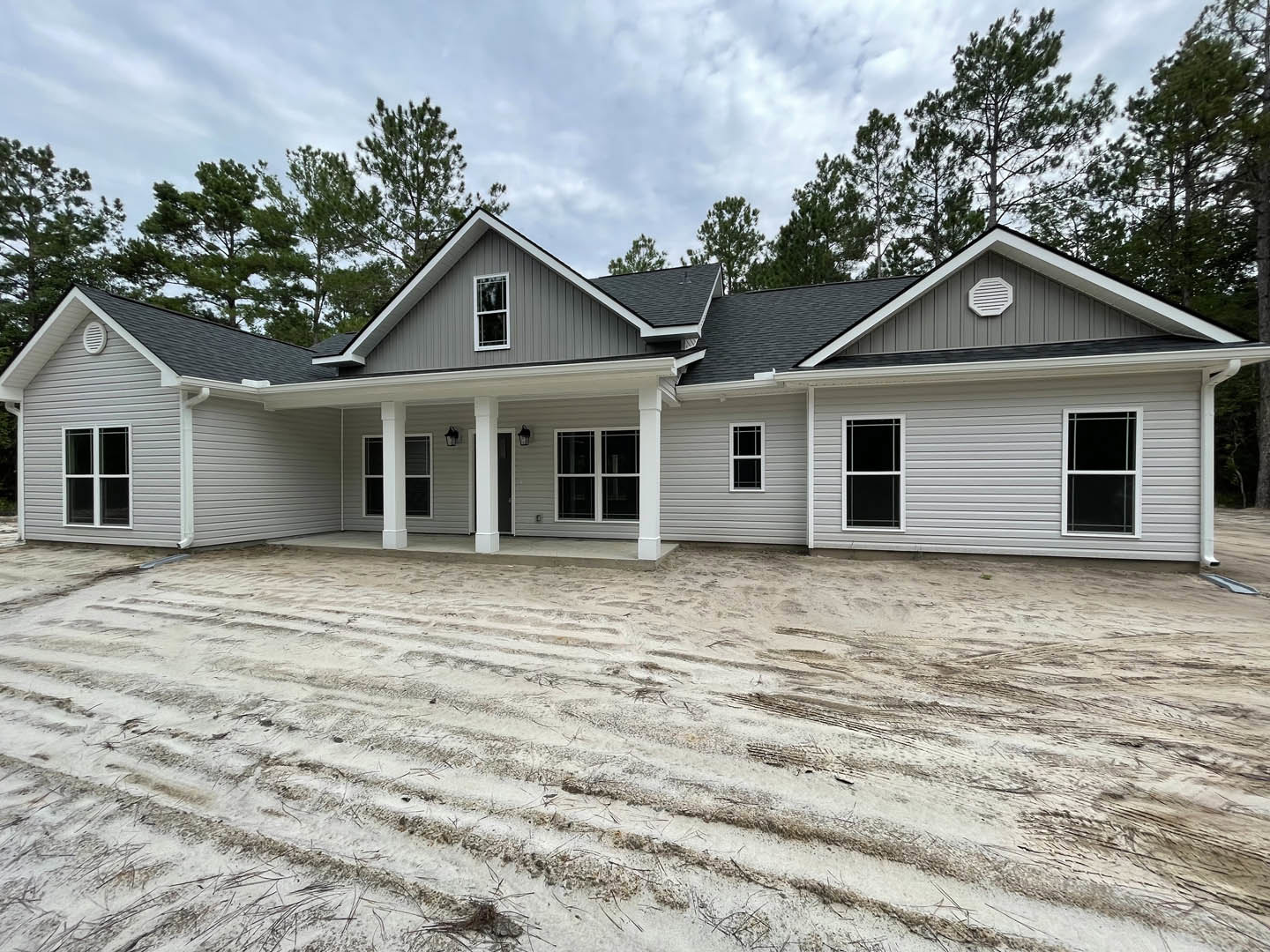 White garage door and screened window on a house with light siding, dirt driveway, covered porch, white wall vent, and cloudy sky.