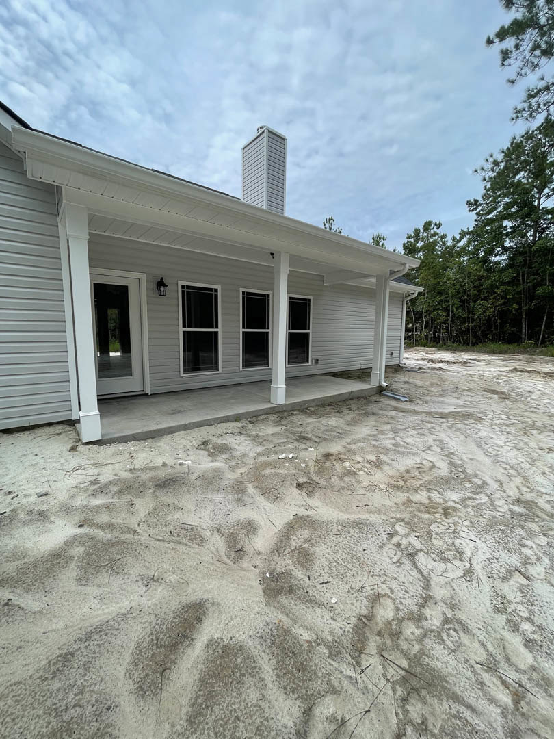 White custom home with prominent brick chimney, sand-covered yard, white-framed windows, and close-up view of entry door.