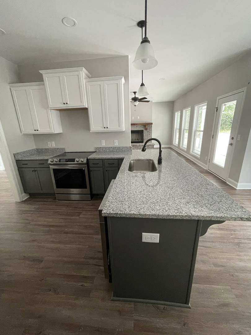 Open-concept kitchen featuring a central island with a black curved-neck faucet and sink, stainless steel stove, white cabinetry, stone countertops, wood flooring, and a