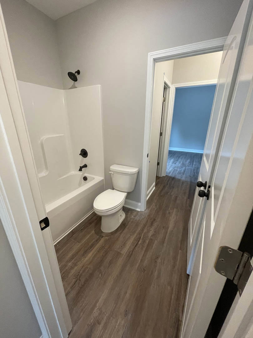Bathroom with white toilet and freestanding white bathtub featuring black faucets, blue wall with white trim, tile floor, and visible door hinge