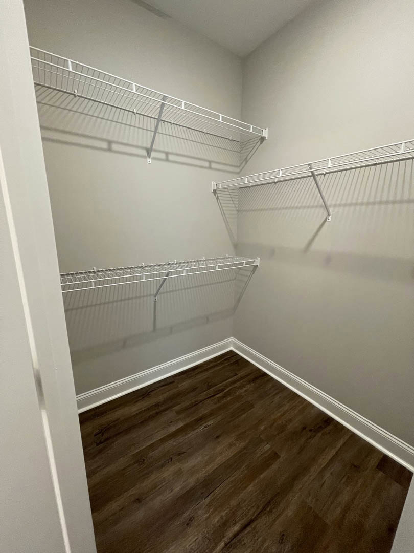 Walk-in closet with white built-in shelves, hardwood flooring, and white baseboards