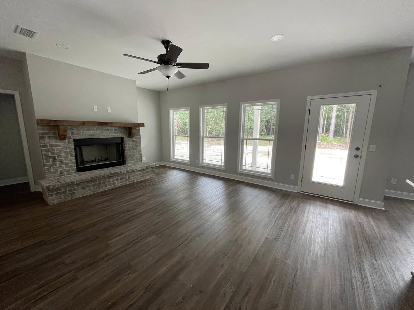 Living room with wood flooring, black-framed fireplace, ceiling fan with light, white-framed windows, and glass-paneled door