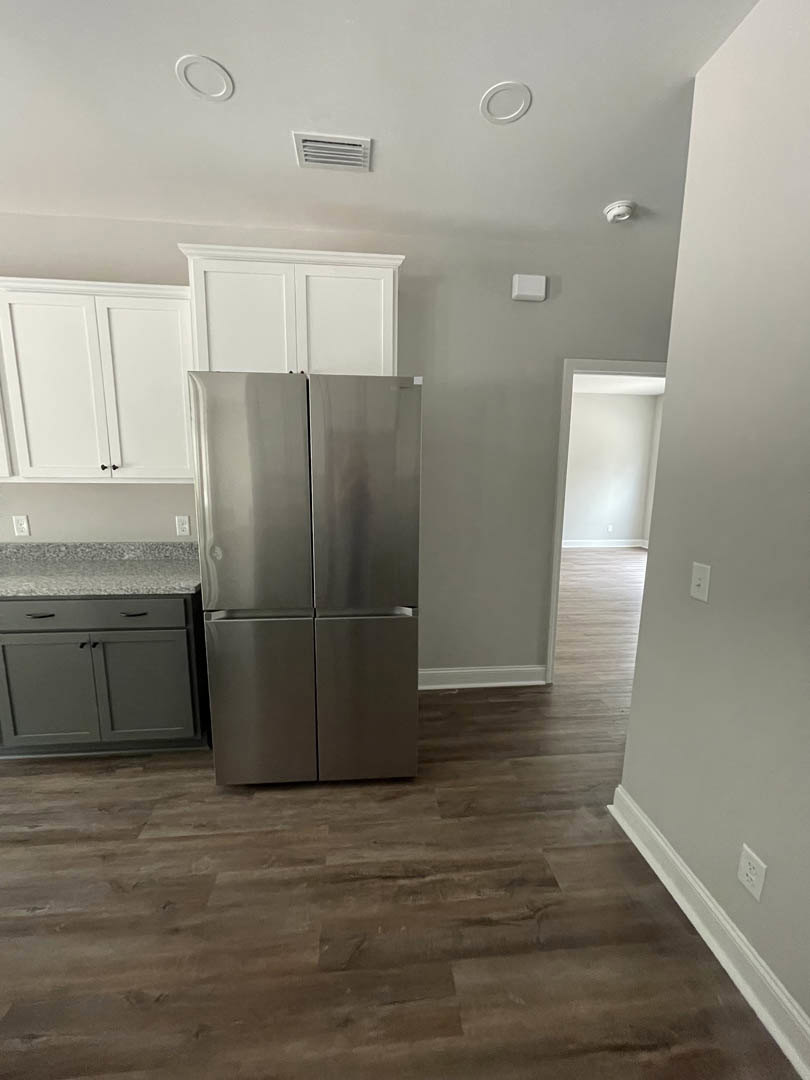 Stainless steel refrigerator beside white cabinetry with black handles, light stone countertops, and wood flooring in a modern kitchen