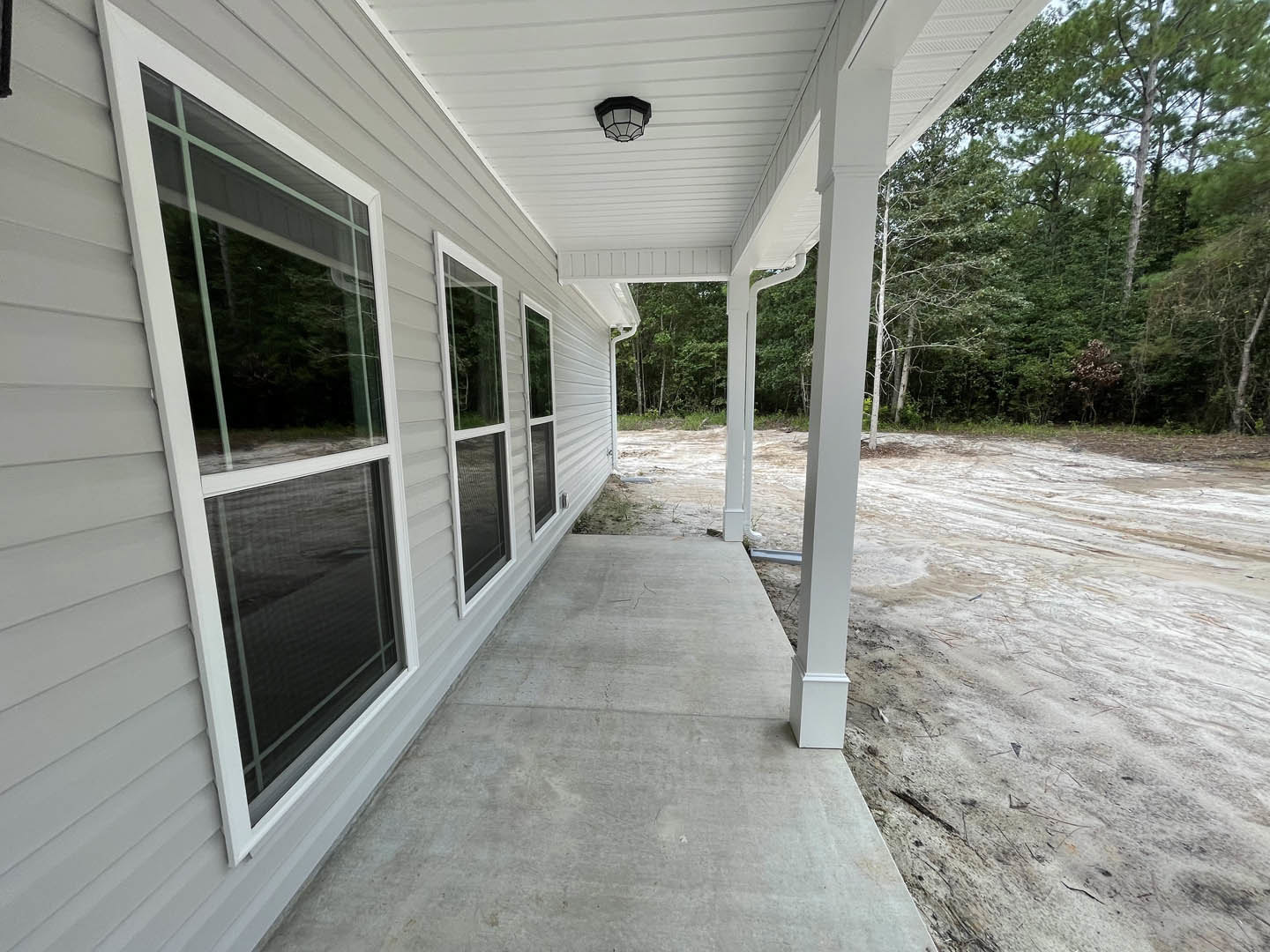 Two-story house with white-framed windows, concrete walkway, and dirt road surrounded by mature trees
