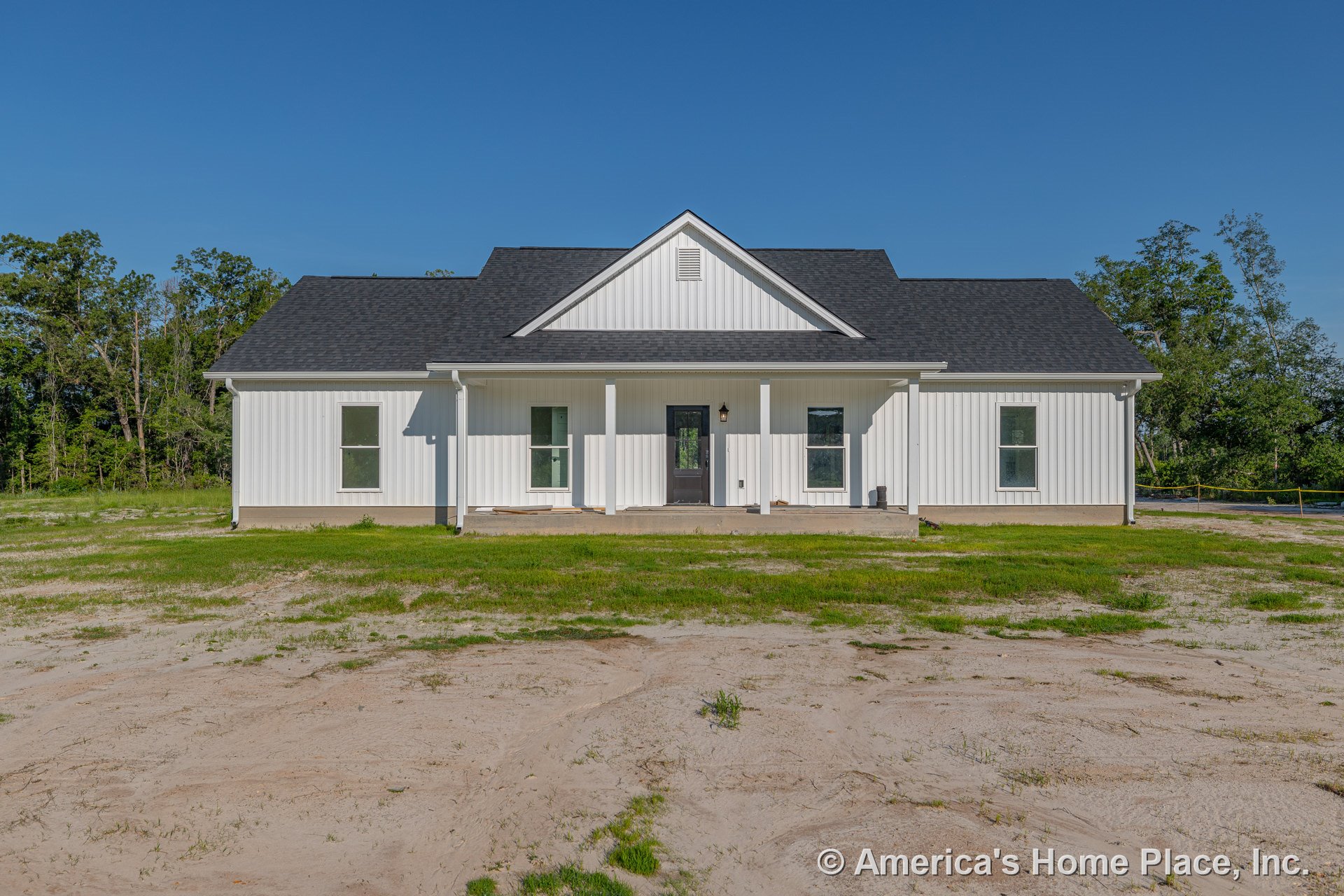 White vertical board and batten siding with black shingle roof, covered front porch, three tall front windows, central front door, and simple exterior trim