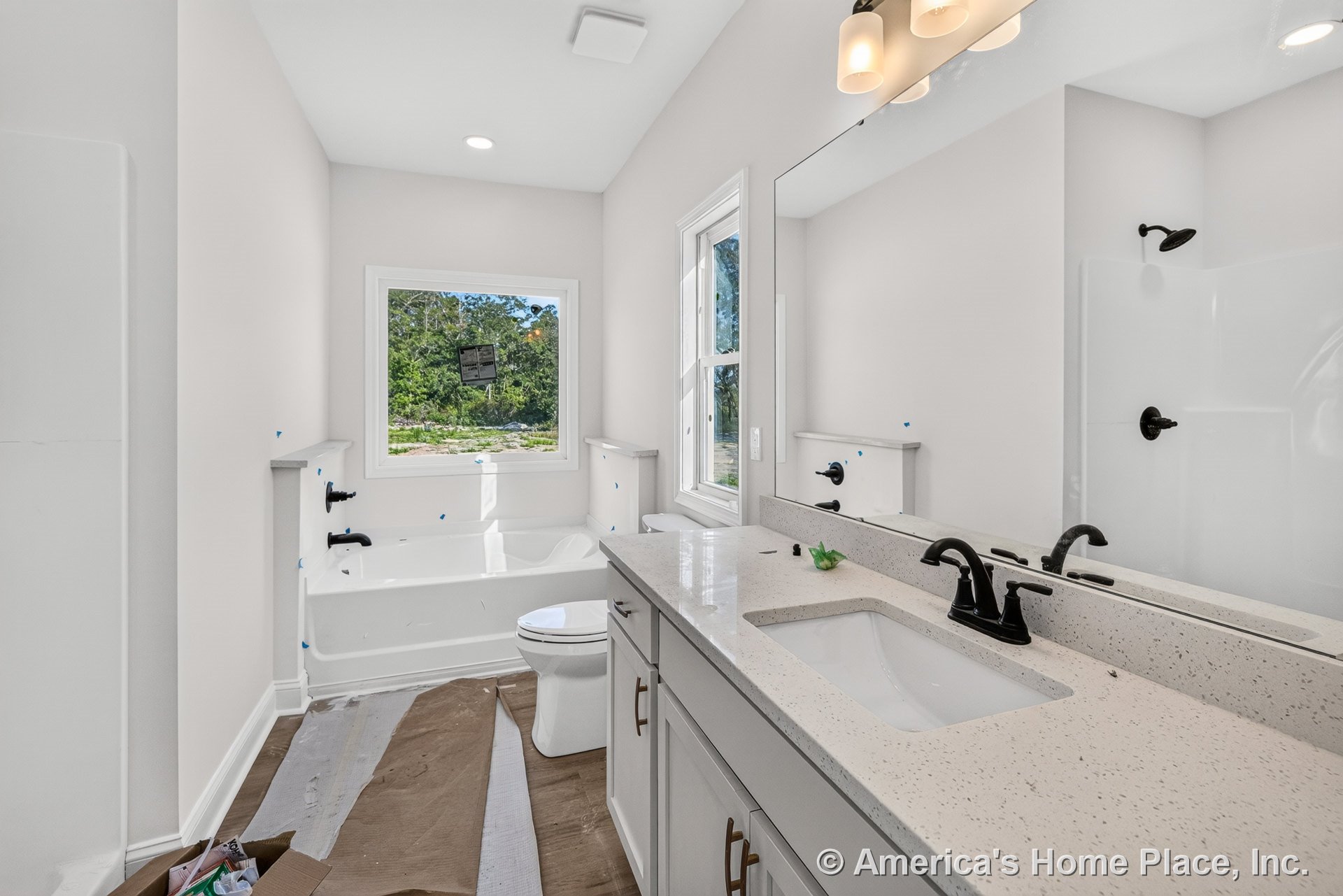 Double vanity with quartz countertop and white shaker cabinetry, soaking tub positioned beneath a large window, walk-in shower featuring black fixtures, expansive mirror, recessed