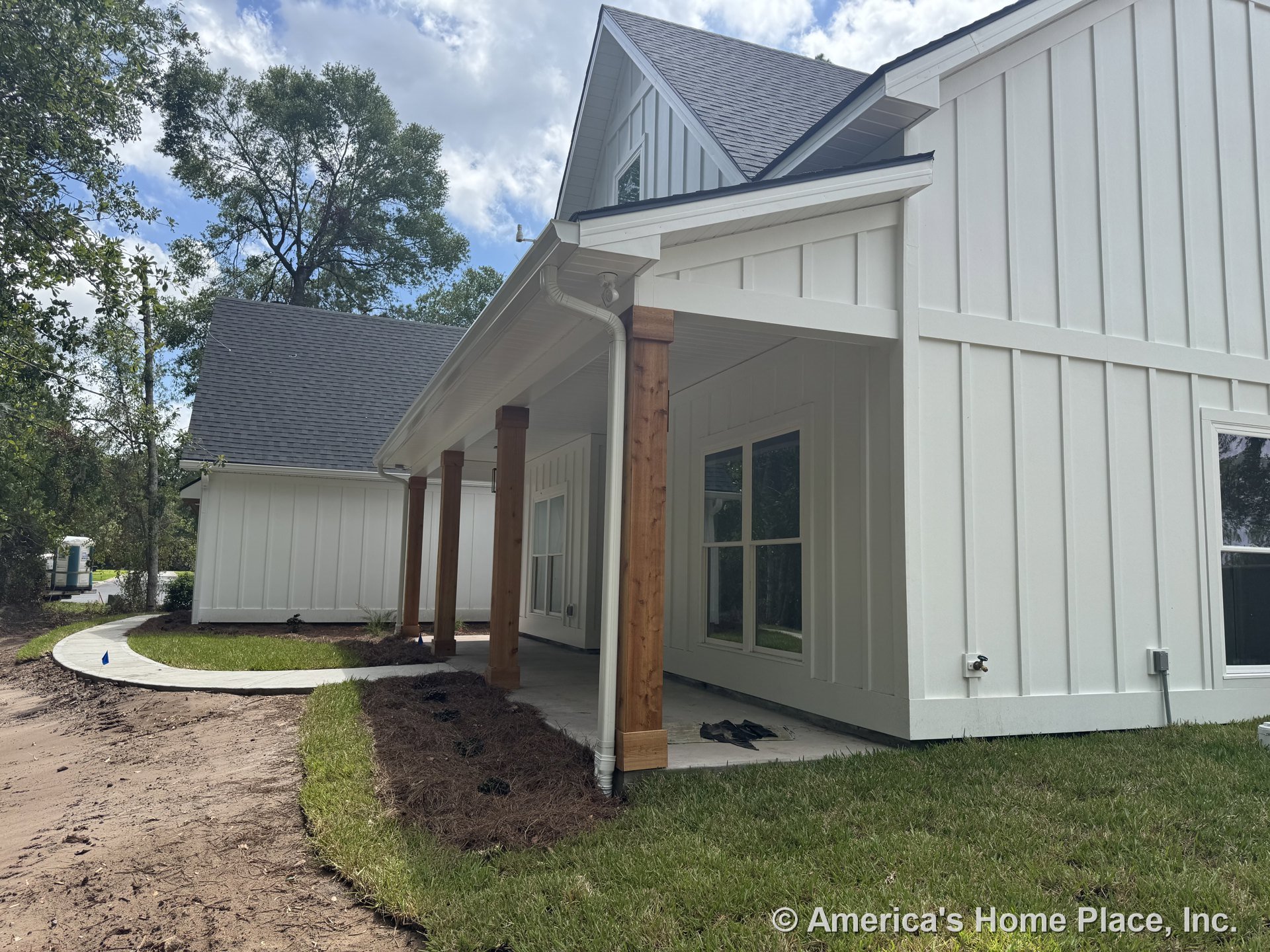 White board and batten siding with a covered porch supported by natural wood columns, concrete walkway, large windows, and asphalt shingle roof.