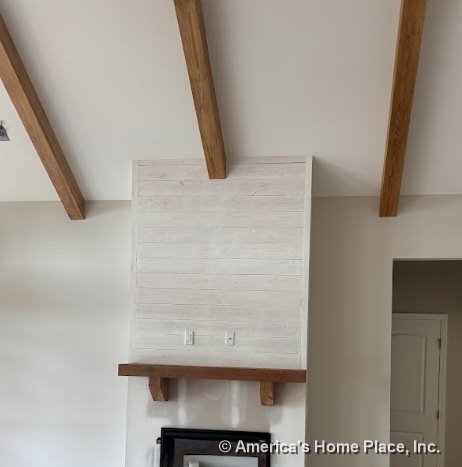 Fireplace with wood mantel and shiplap accent wall beneath vaulted ceiling with exposed wood beams, neutral paint, built-in electrical outlets, and detailed trim.