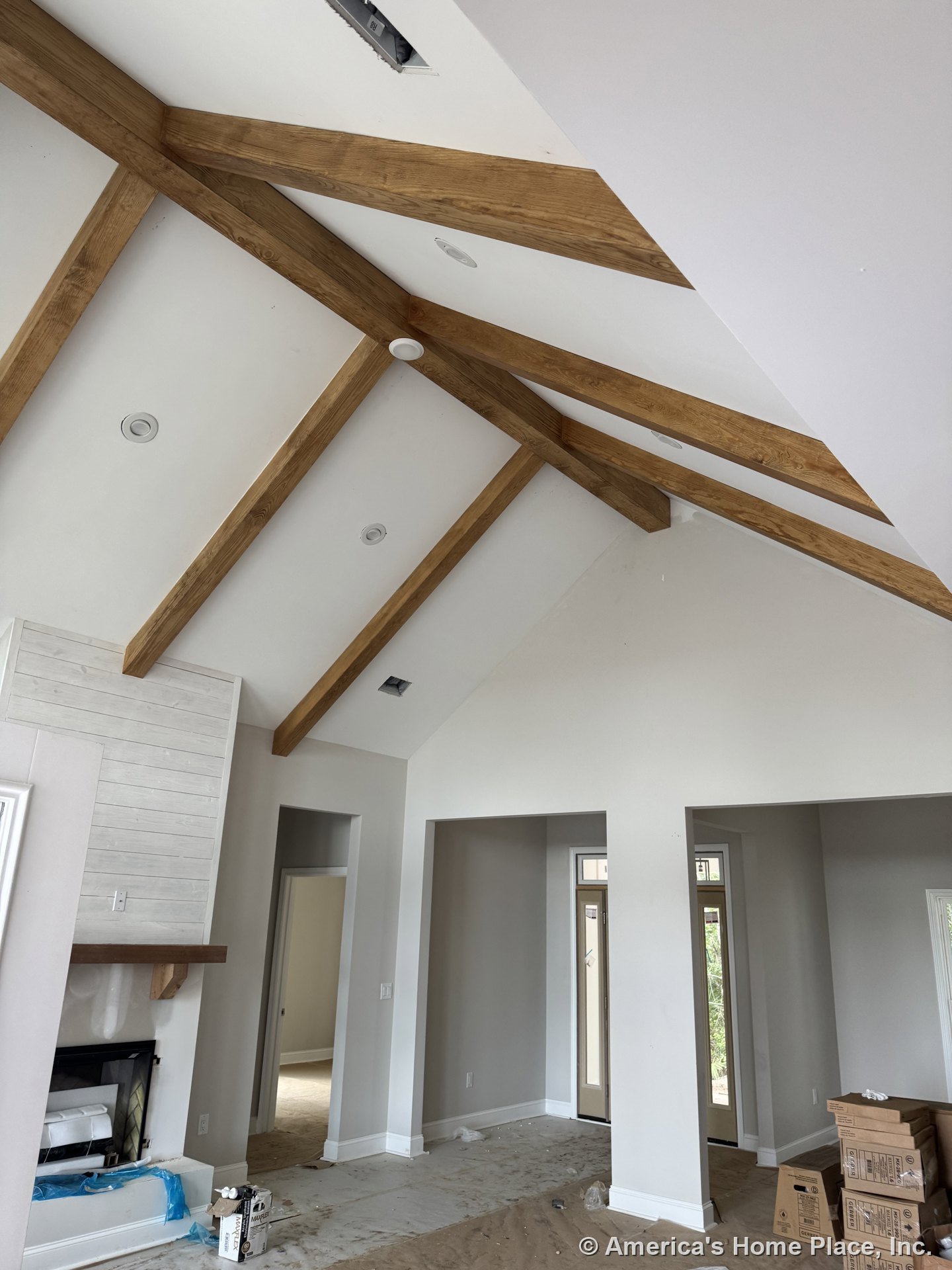 Vaulted living room ceiling with exposed wood beams, built-in fireplace framed by shiplap trim, large entryway featuring transom windows, neutral painted walls, white baseboard