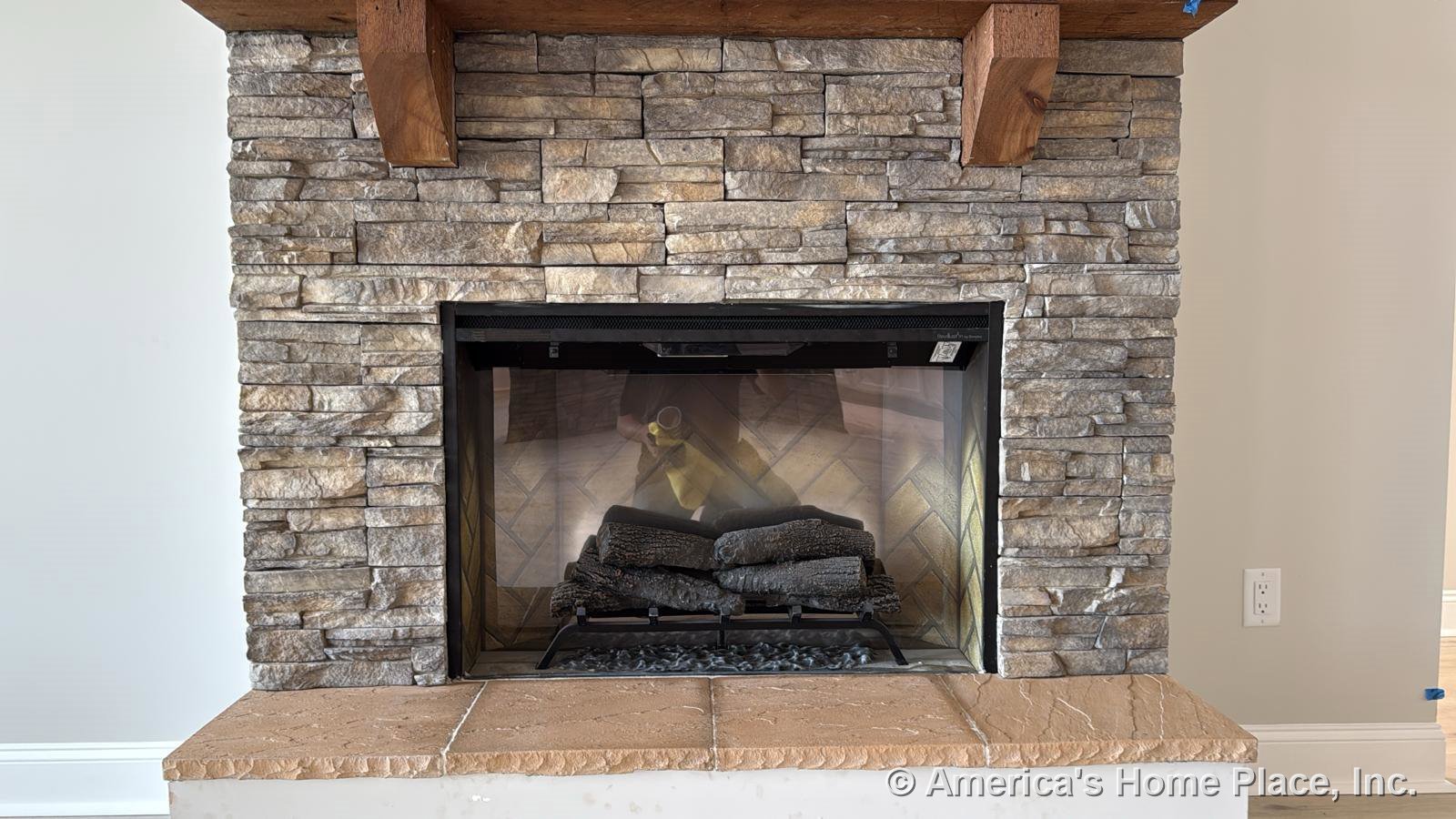 Stone veneer fireplace with wood beam mantel and tile hearth, gas insert, neutral painted walls, white baseboard trim, finished flooring in custom living room.