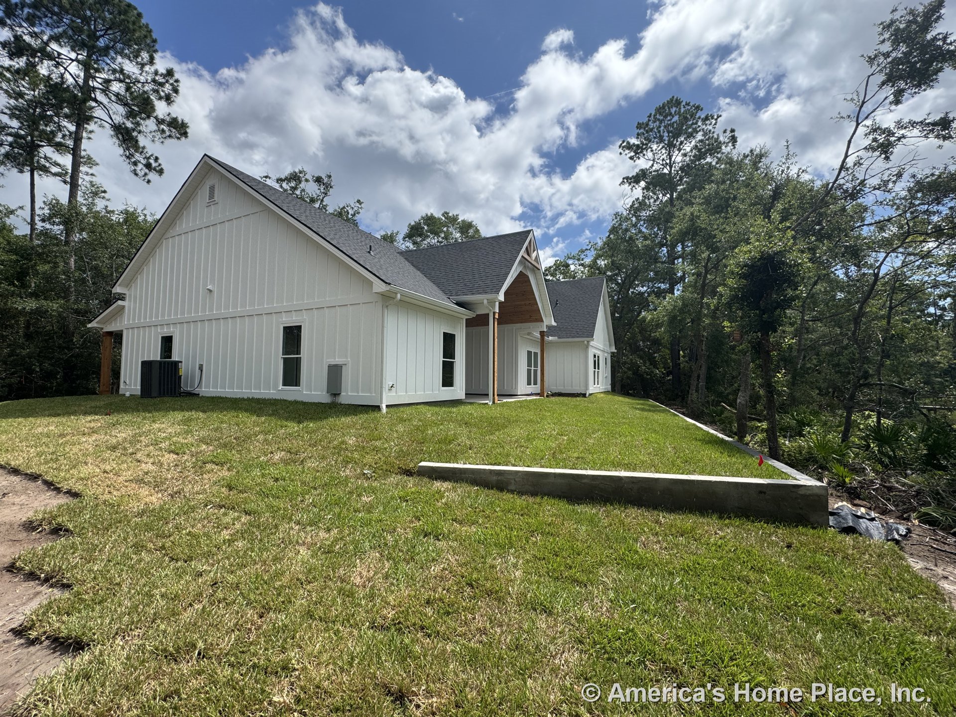 White board and batten siding with trimmed roof edges, multiple gable rooflines, covered entry porch featuring wood ceiling, double-hung windows, concrete retaining wall, and