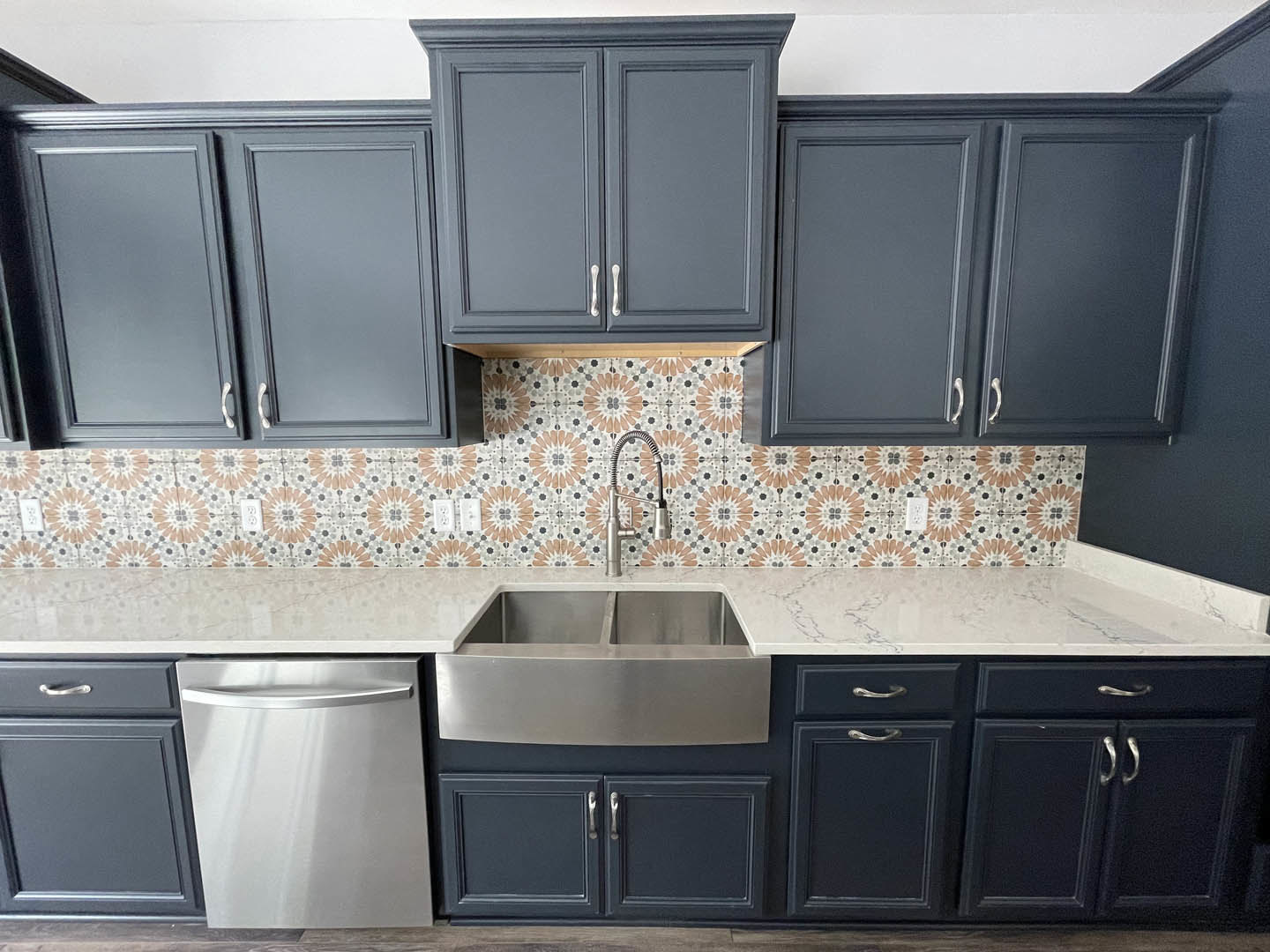 White quartz countertop with stainless steel sink, stainless steel dishwasher with handle, grey cabinetry with silver handles, close-up of backsplash tile