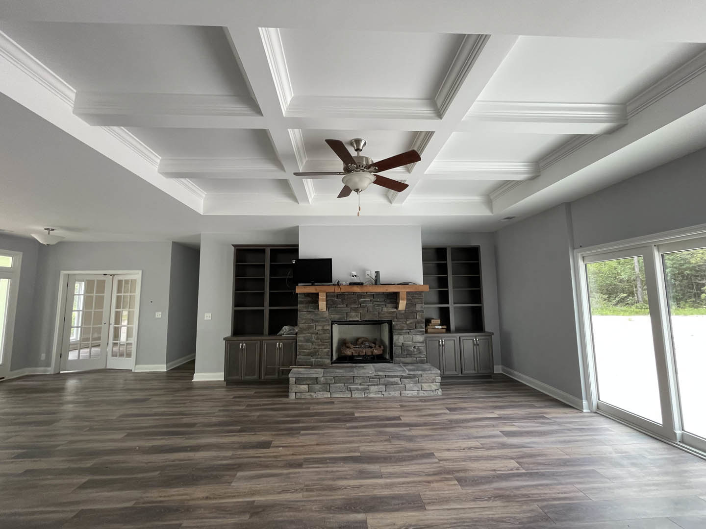 Living room with wood flooring, stone fireplace containing logs, ceiling fan with light fixture, and white double doors with glass panes.