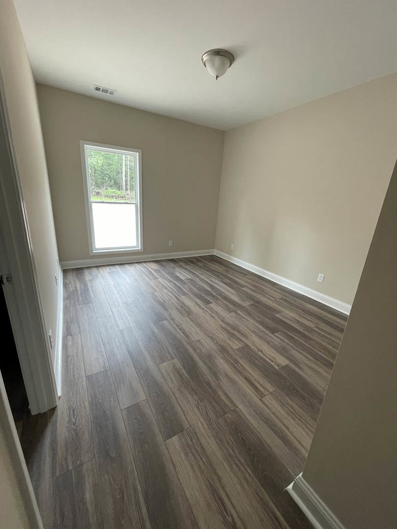 Wood floor with sunlight, white trimmed walls, ceiling light fixture, large window overlooking trees
