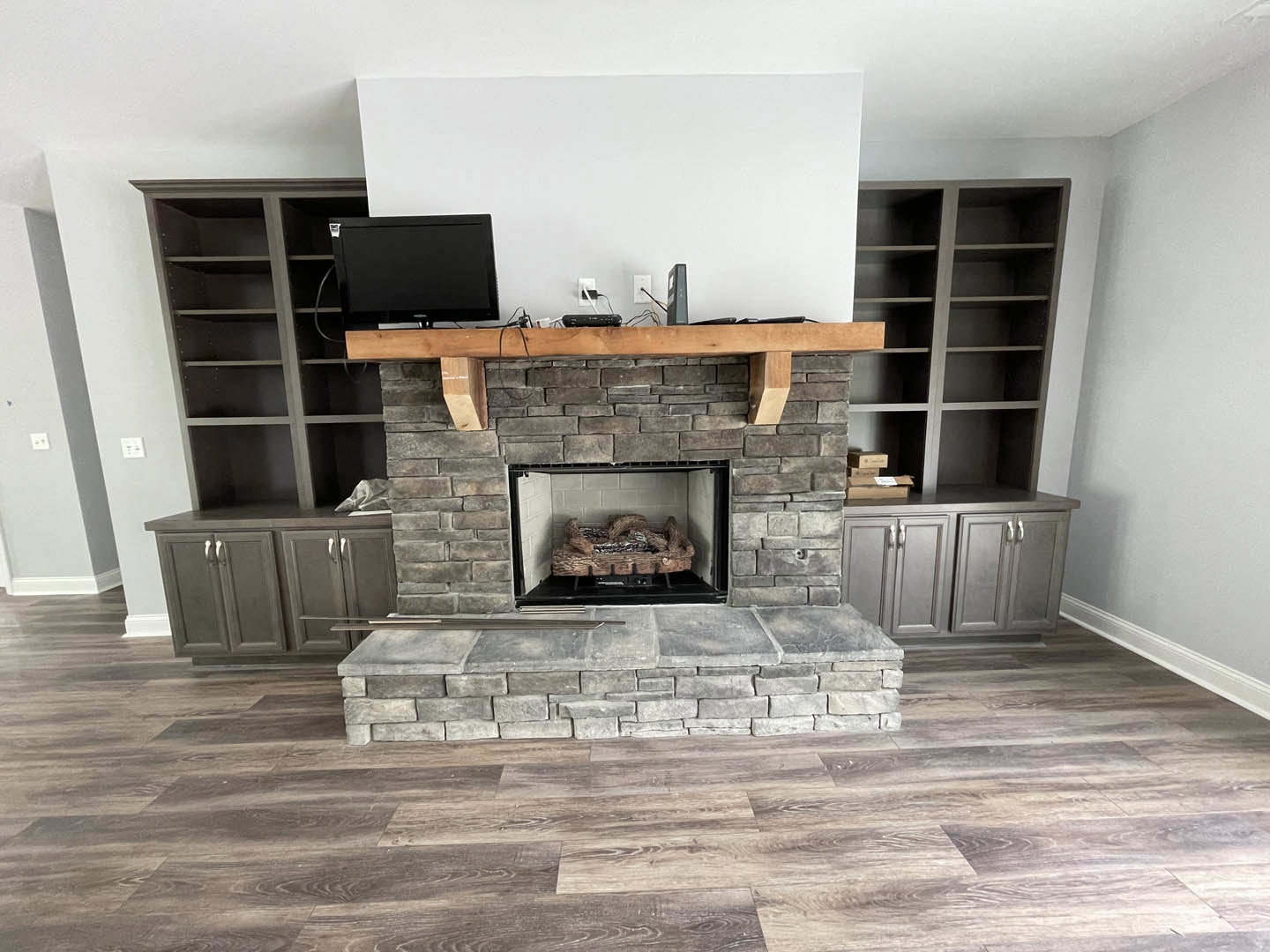 Stone fireplace with black metal frame, wood log burning inside, built-in shelves on either side, hardwood floor, neutral walls, cozy den interior