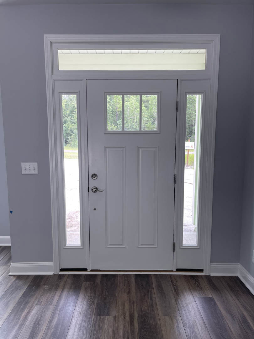 White door with glass panes, dark wood flooring, white walls, window showing trees outside, multi-switch light panel