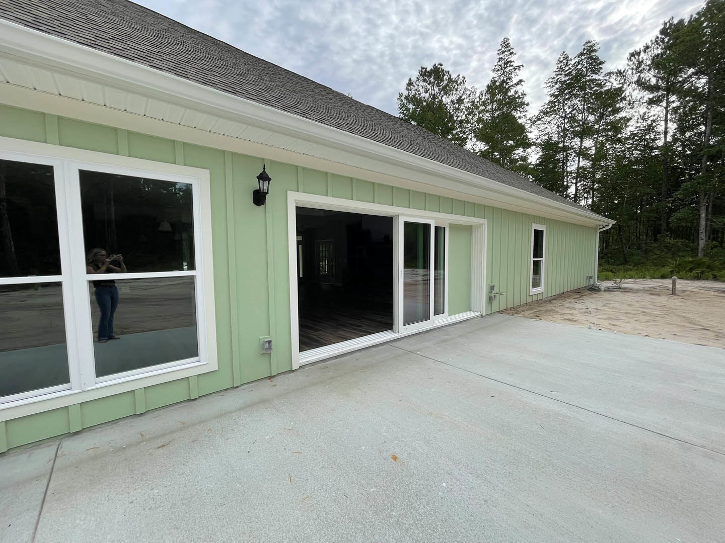 Modern house exterior with green siding, white-framed windows, attached garage, concrete driveway, and a person standing near the entrance.