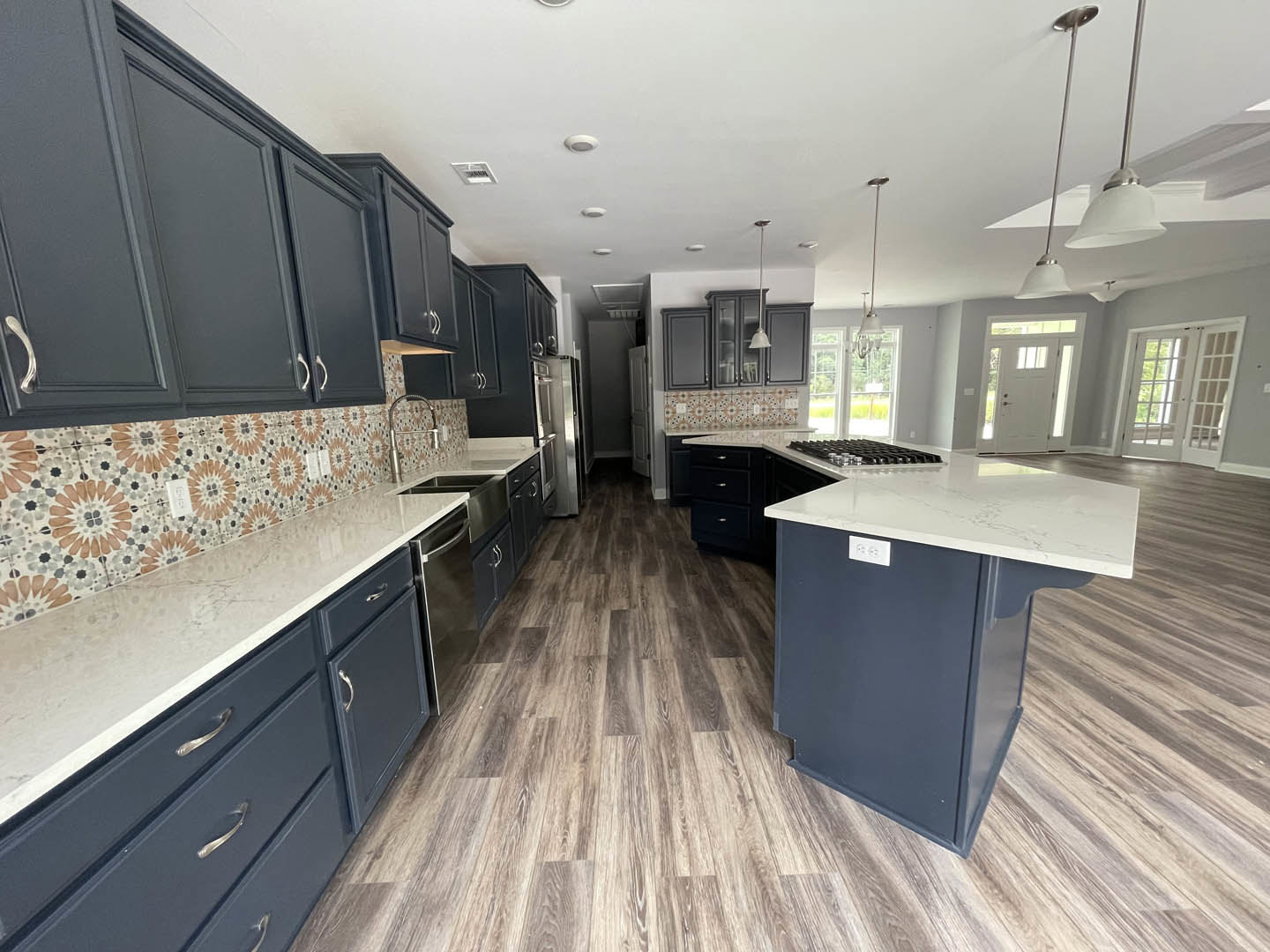 Spacious kitchen featuring a large marble-topped island, white cabinetry, stainless steel sink, and double doors with glass windows.