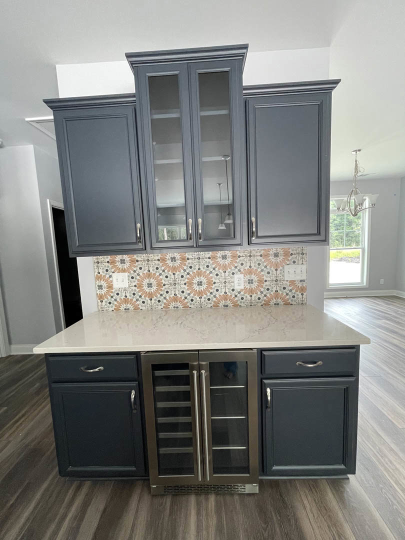 Grey shaker cabinets with brushed nickel hardware, white quartz countertop, stainless steel refrigerator, floral wallpaper accent above counter, white subway tile backsplash