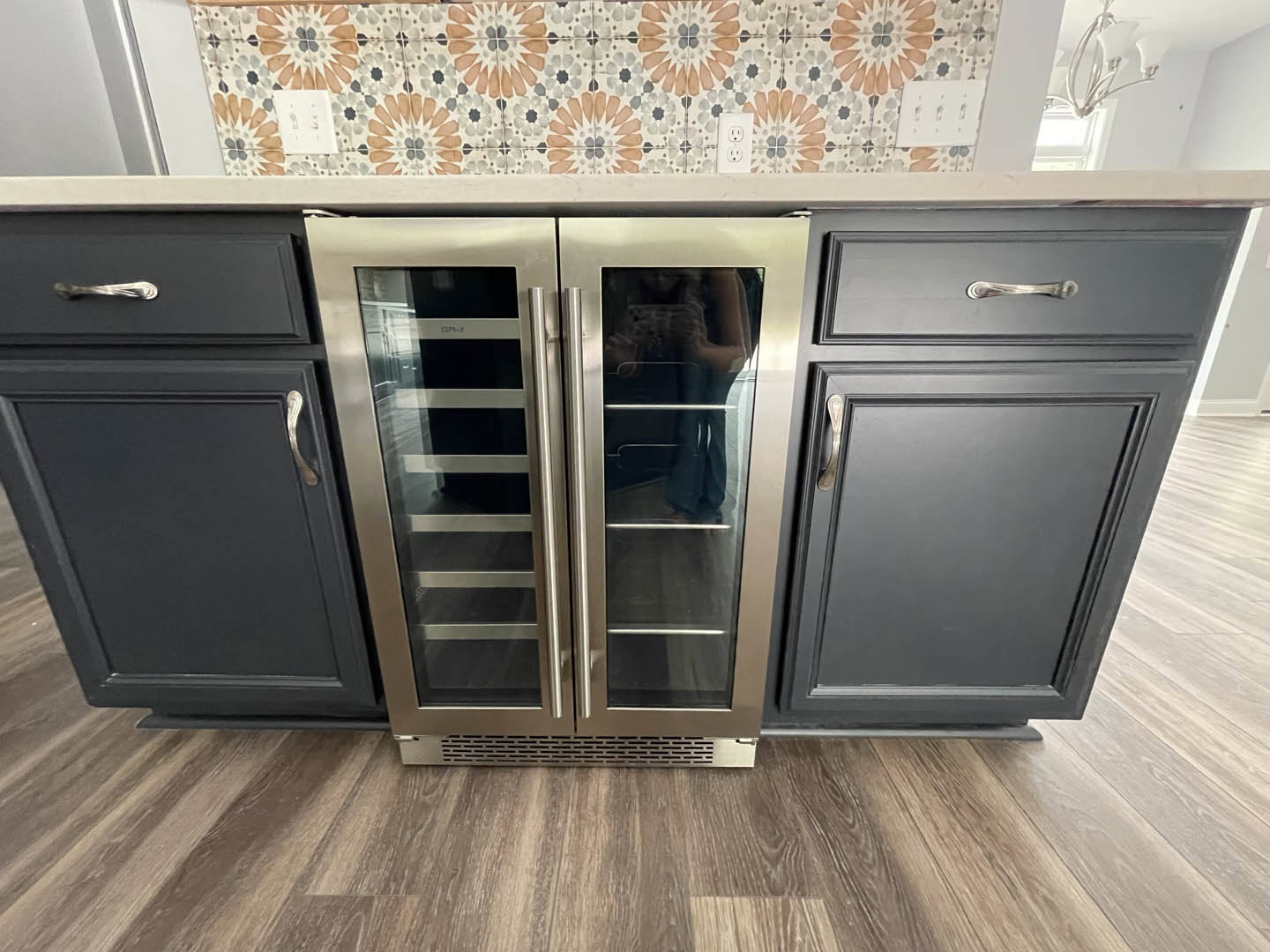 Stainless steel double door refrigerator with glass doors, black cabinets with silver handles, tile flooring, and white countertops in a modern kitchen