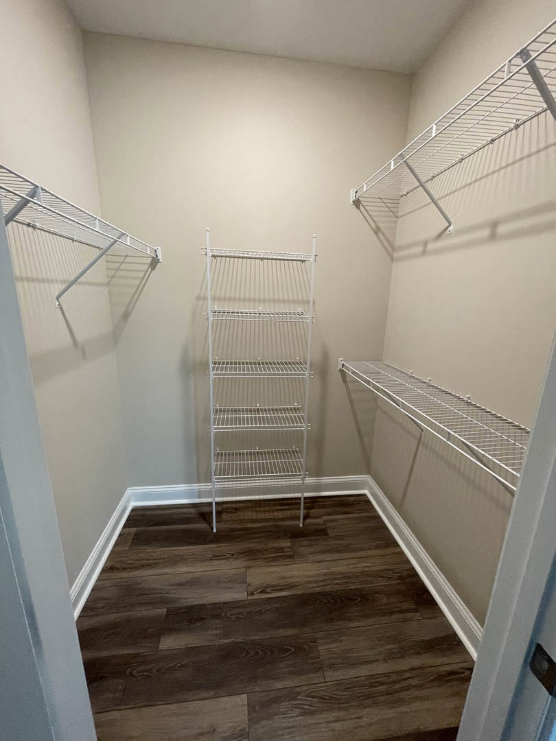Walk-in closet with white metal shelving, wood plank flooring, plaster walls, and ceiling.