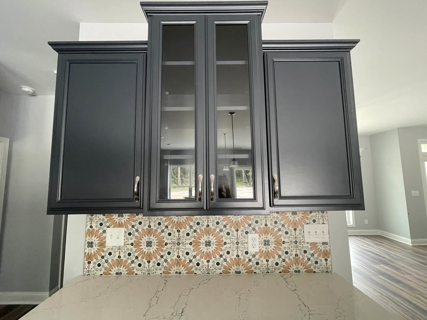 Kitchen with matte black cabinets, patterned tile backsplash, glass cabinet doors, wood flooring, and white walls