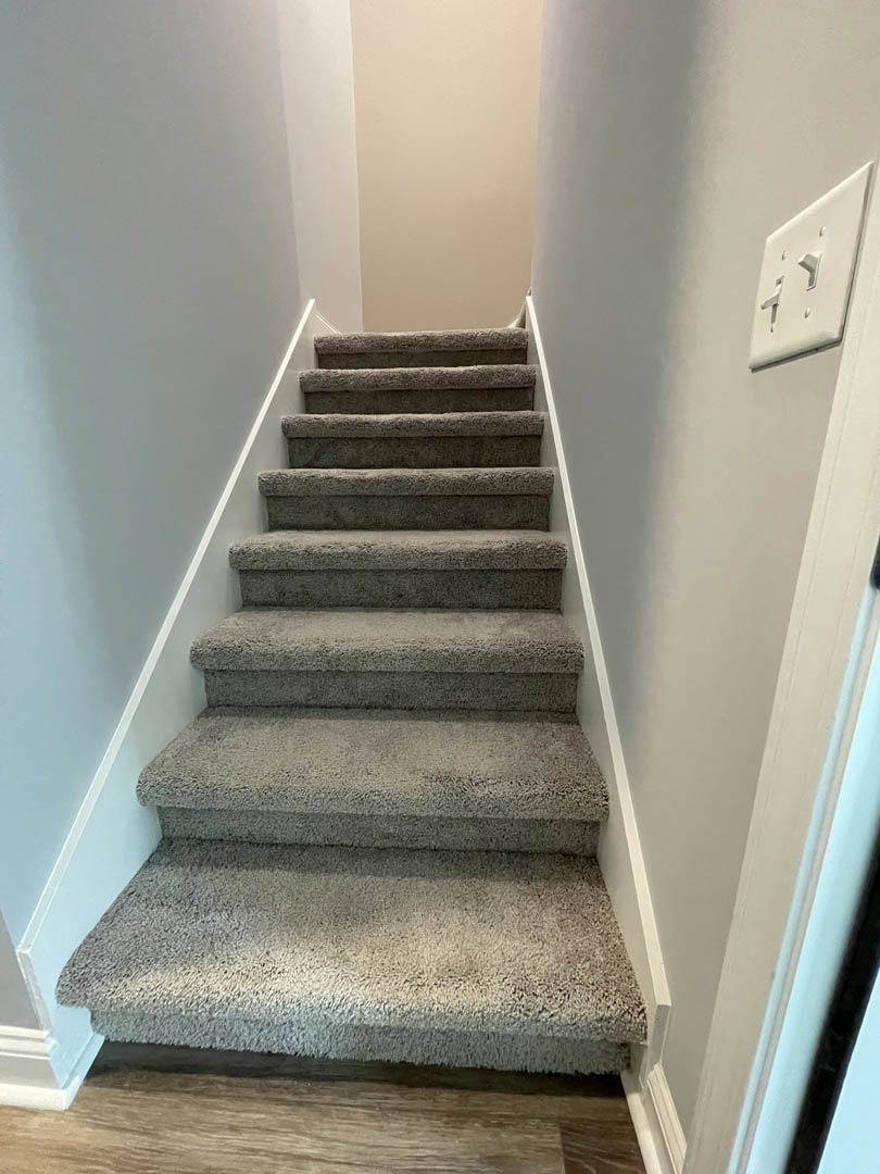 Carpeted staircase with wooden handrail, plaster walls, and grey carpeting on steps