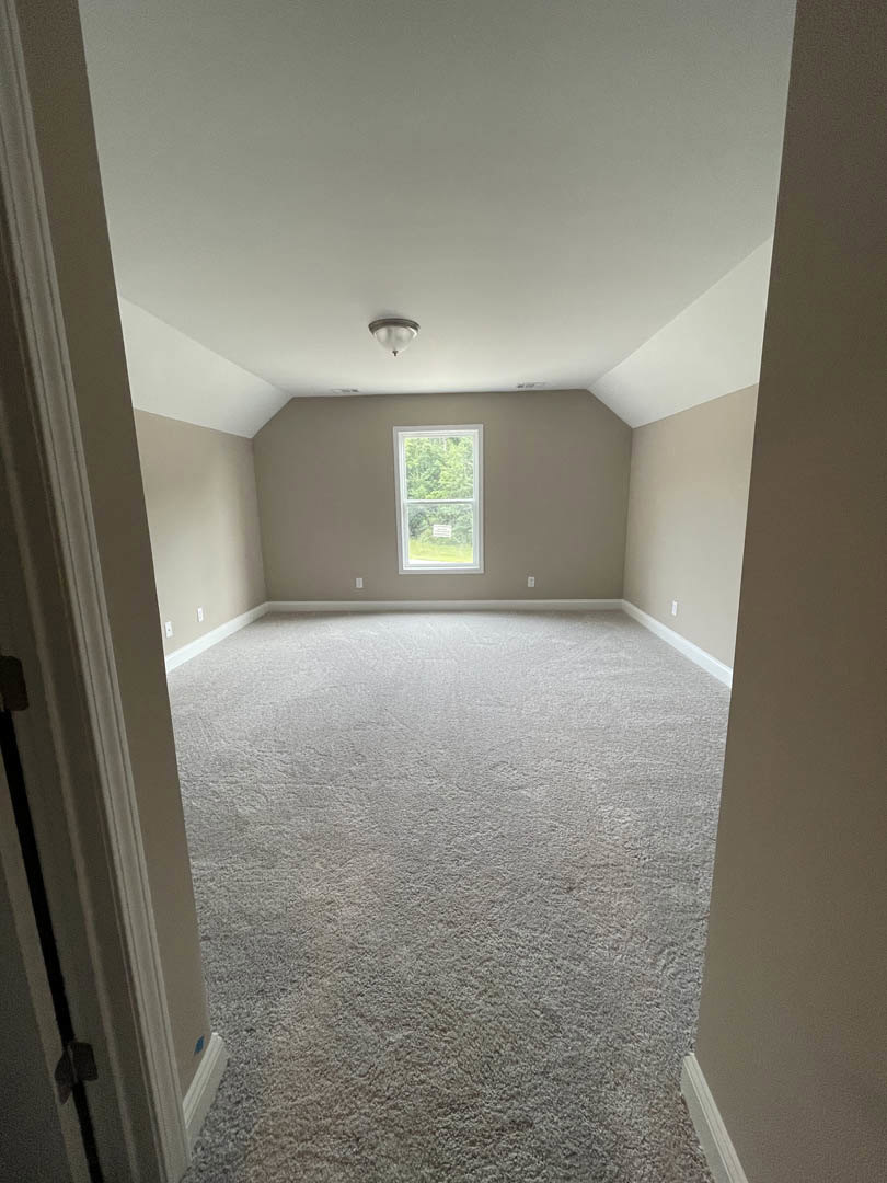 Carpeted room with white walls, black trim, ceiling light fixture, and window displaying a sign
