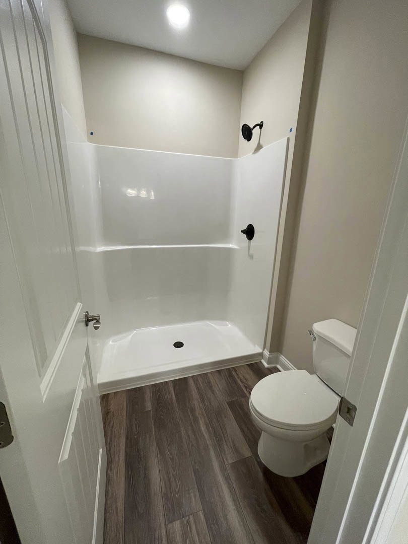 Modern bathroom featuring white tile walls, a toilet with lid up, glass-enclosed shower, chrome plumbing fixtures, and black wall-mounted accessory.