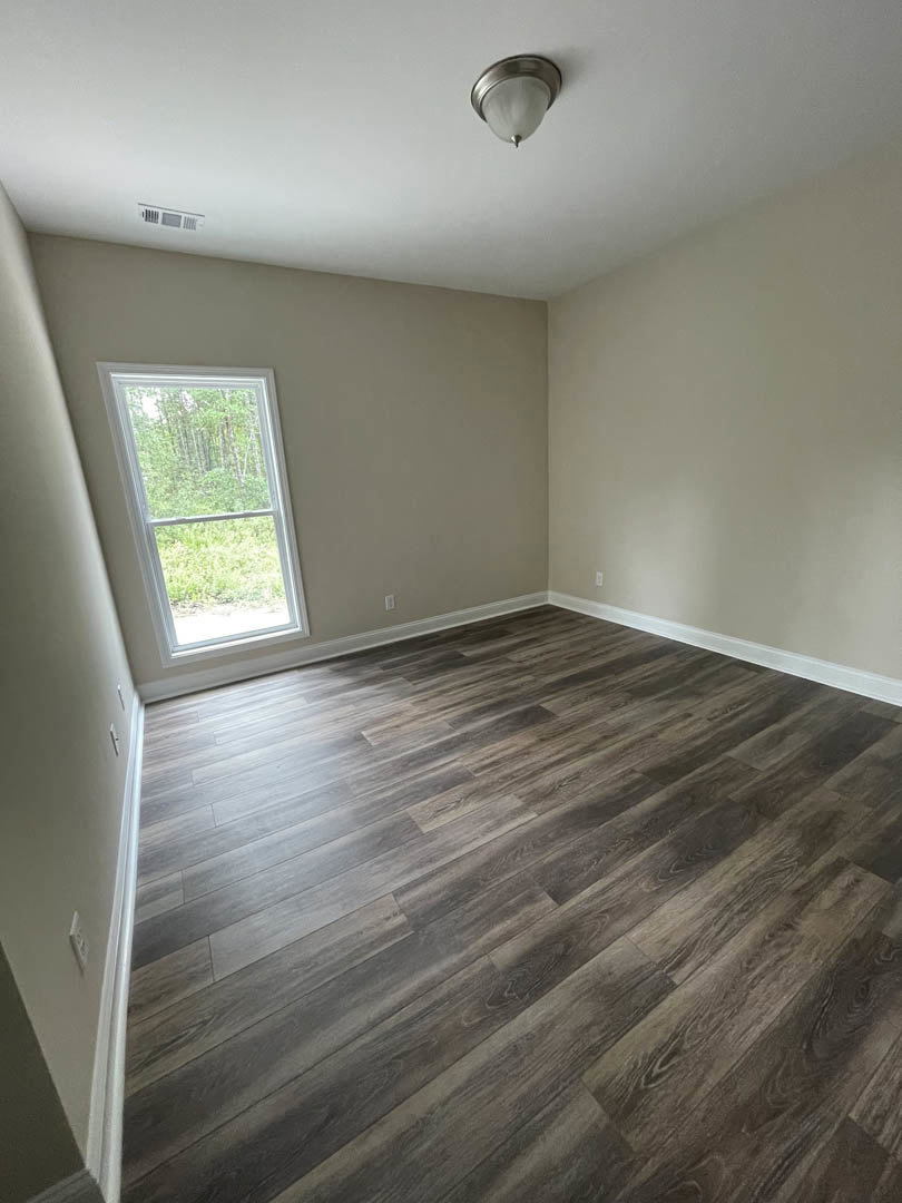 Wood floor room with large window overlooking trees, white plaster walls, ceiling-mounted light fixture